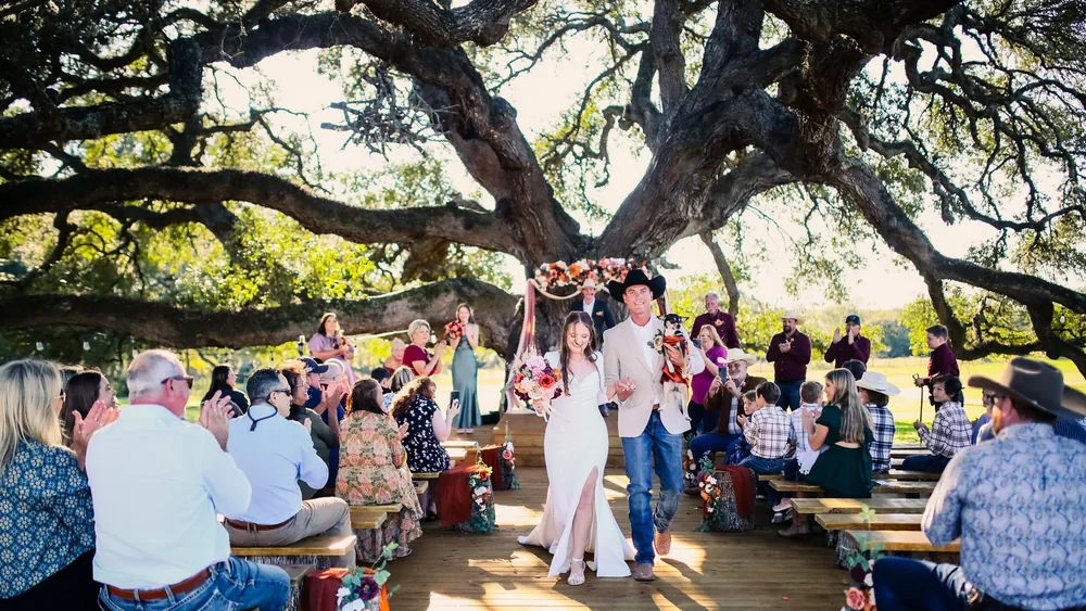 A bride and groom walking the aisle under the great oak